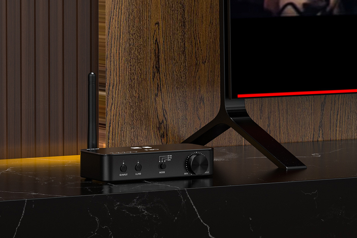 Czarny odbiornik audio z anteną i pokrętłem stoi na stole obok telewizora.