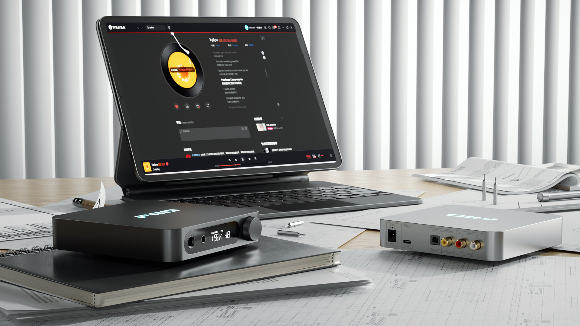 Tablet z aplikacją muzyczną, dwa urządzenia audio i dokumenty na drewnianym biurku przed żaluzjami.