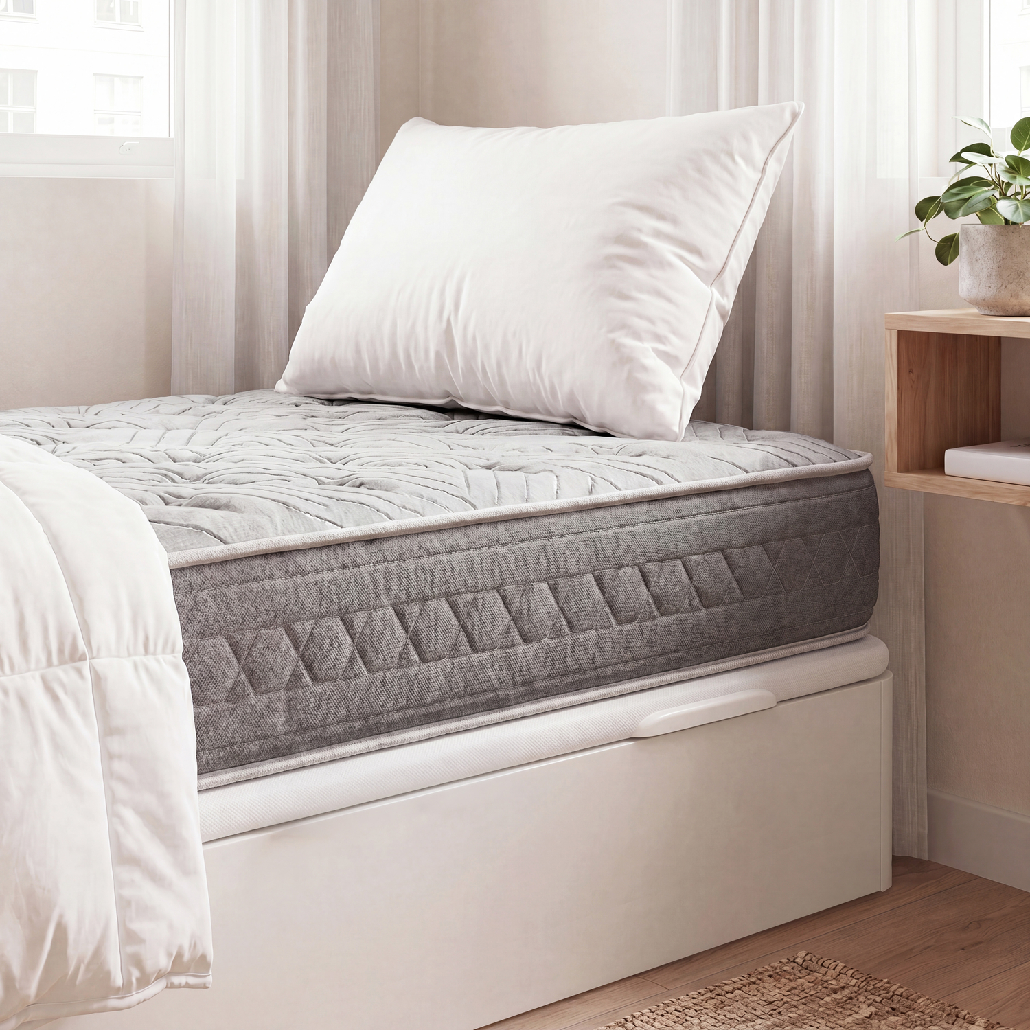 Un colchón gris con almohada y manta blancas en una habitación luminosa.