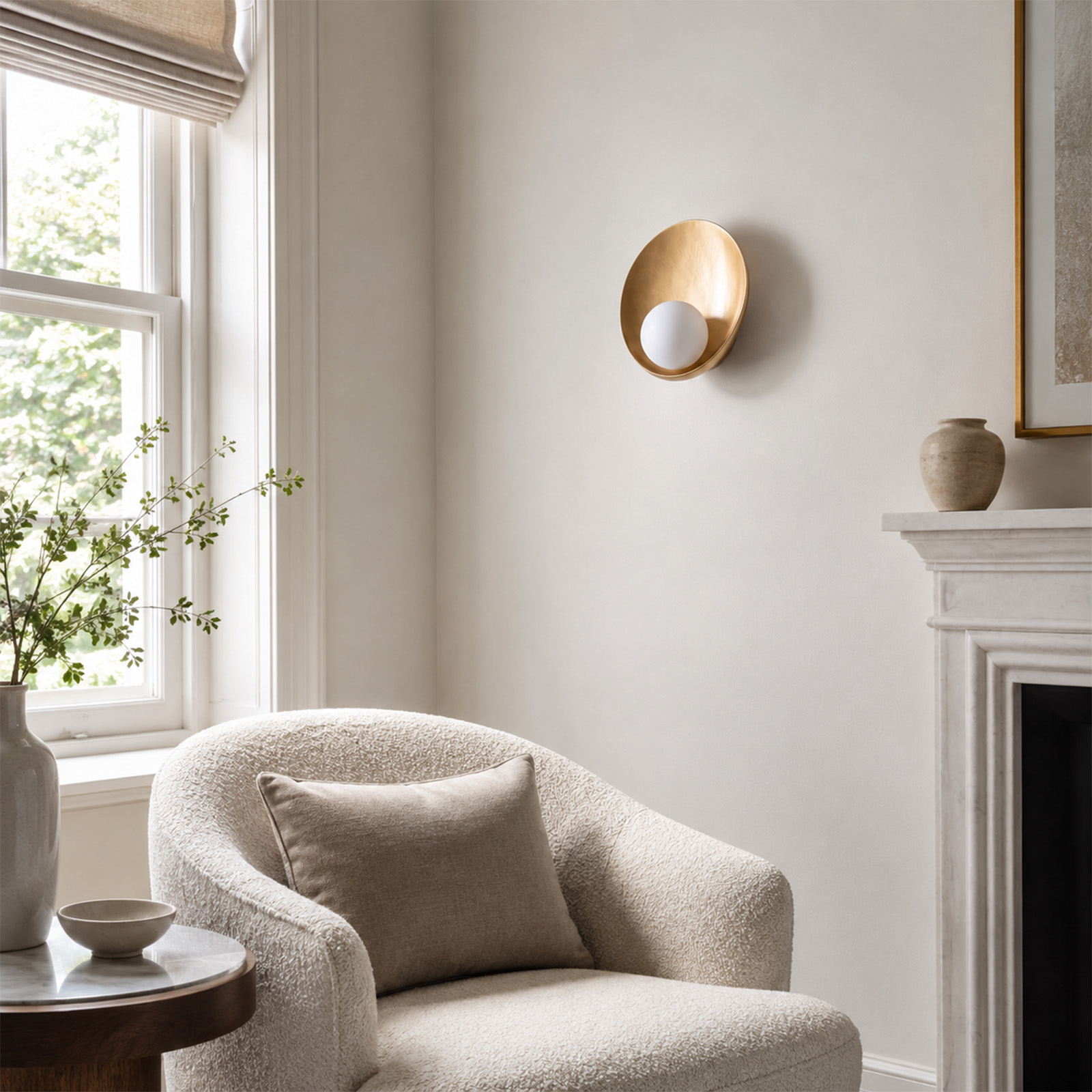 Un sillón blanco de bouclé con cojín frente a una pared clara con aplique dorado y chimenea.