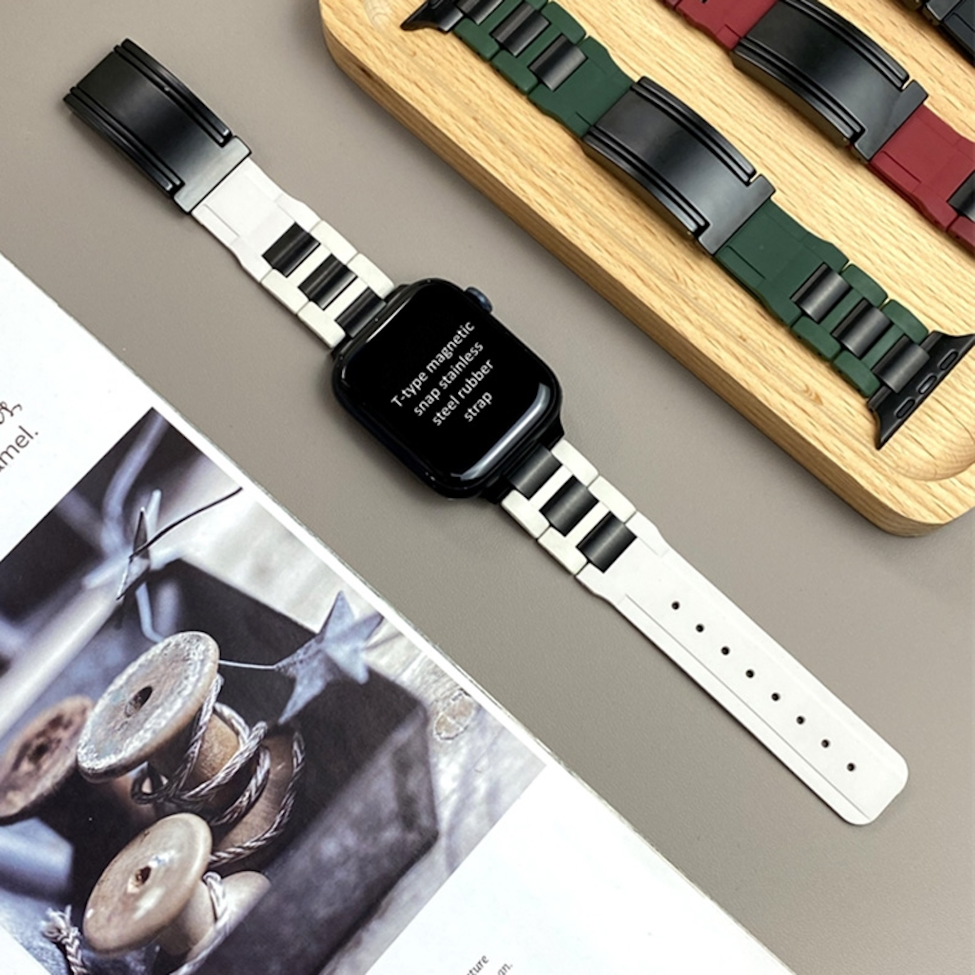 Eine Smartwatch mit weiß-schwarzem Armband auf einer Zeitschrift, neben einem Holztablett.