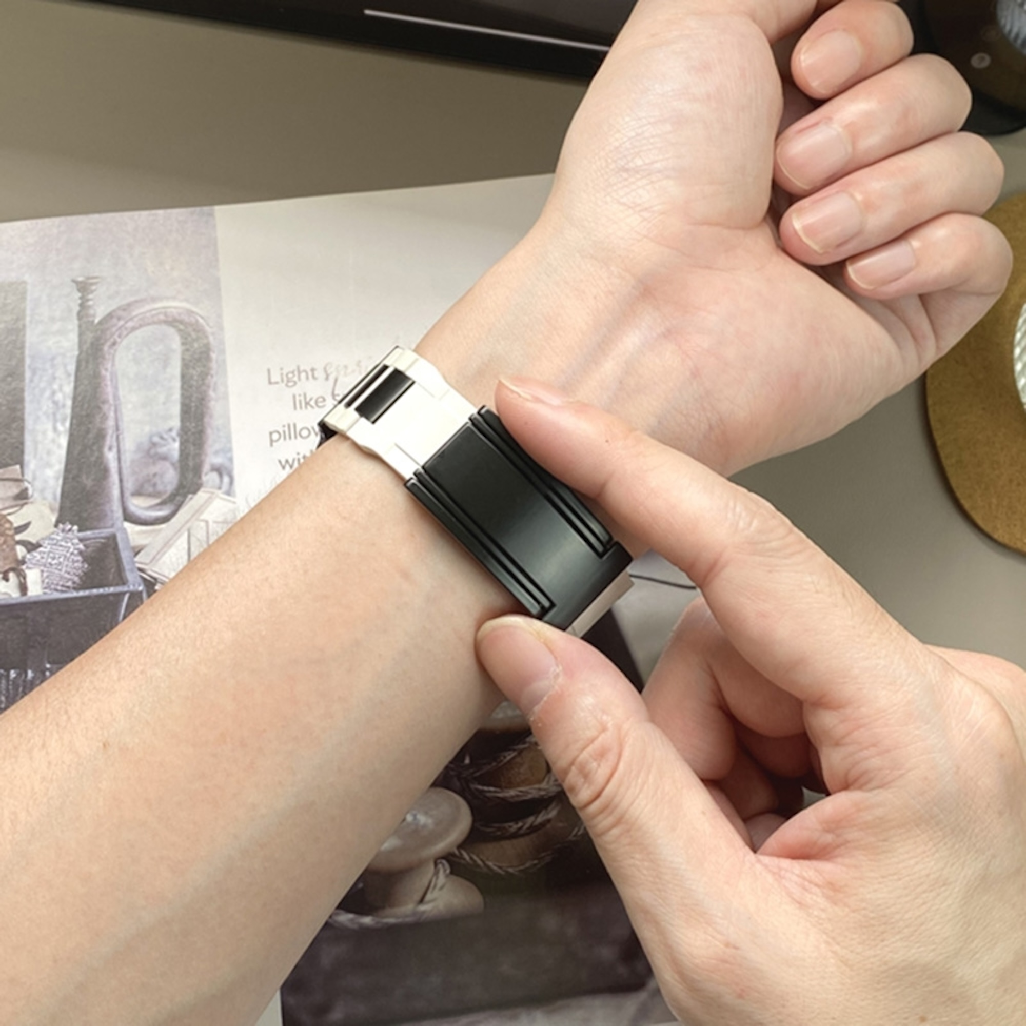 Handgelenk mit einer schwarz-weißen Smartwatch, die von Händen berührt wird.