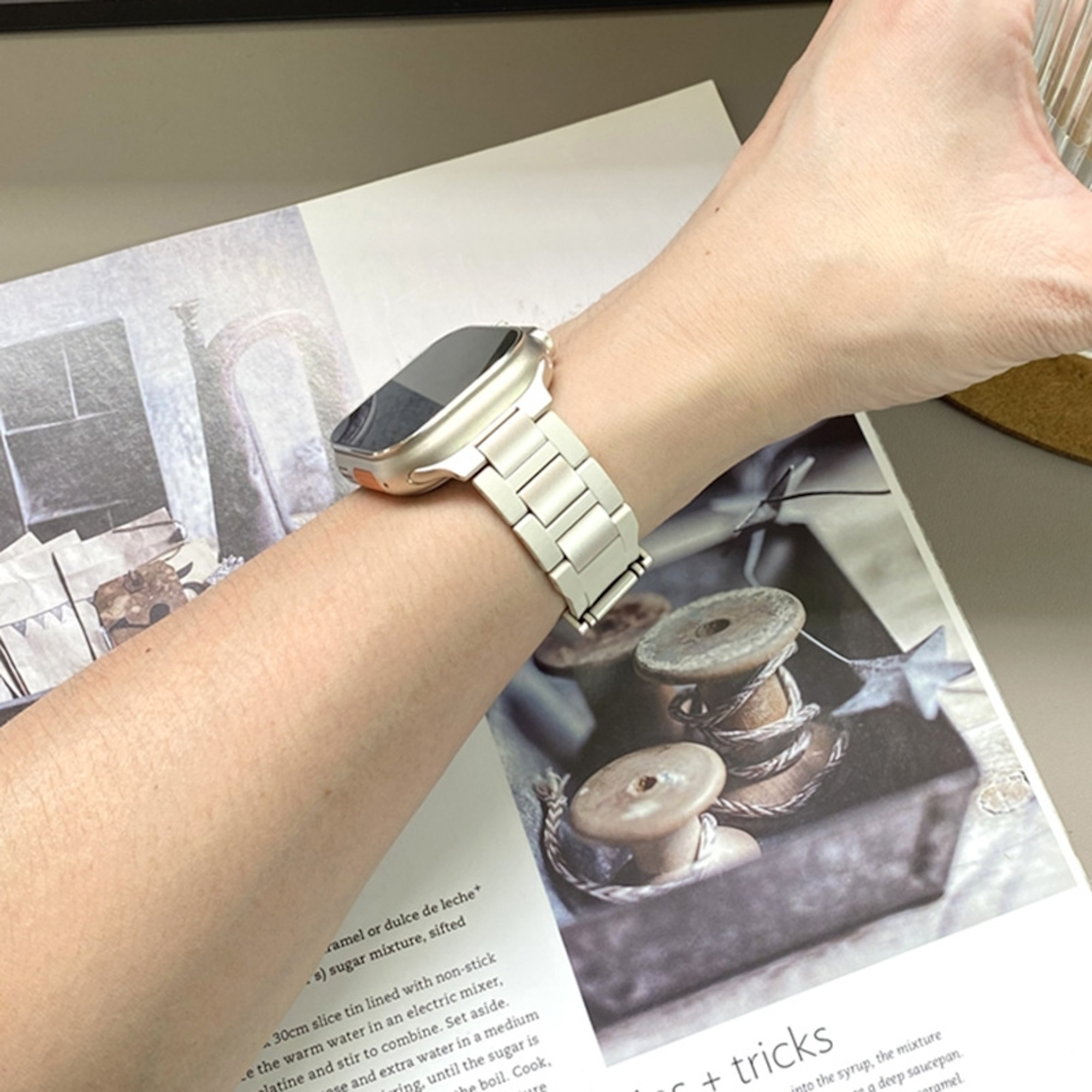 Eine Smartwatch mit silbernem Metallarmband am Handgelenk einer Person über einem Magazin.