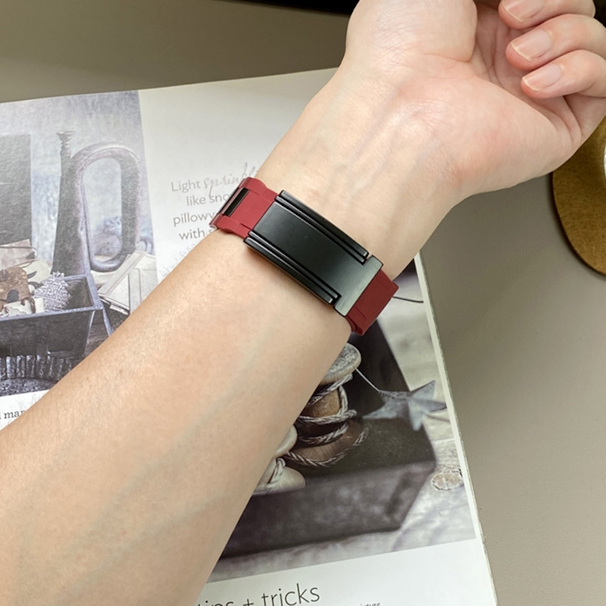 Arm mit rotem und schwarzem Fitnessarmband auf einer Zeitschrift.