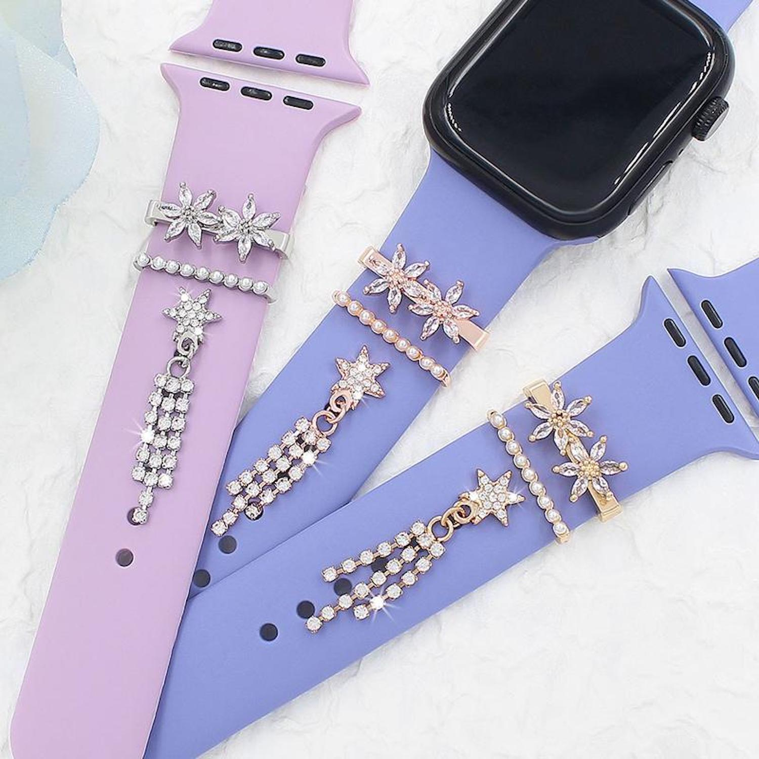Drei lila Silikon-Uhrenarmbänder mit Silber- und Goldanhängern aus Blumen, Perlen und hängenden Sternen.