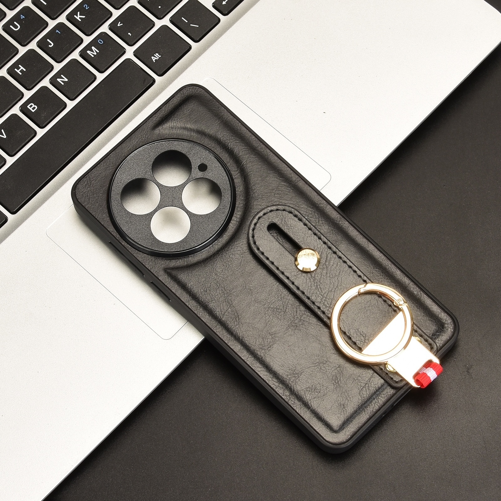 Funda de teléfono de cuero negro con soporte de anillo dorado sobre portátil y mesa negra.