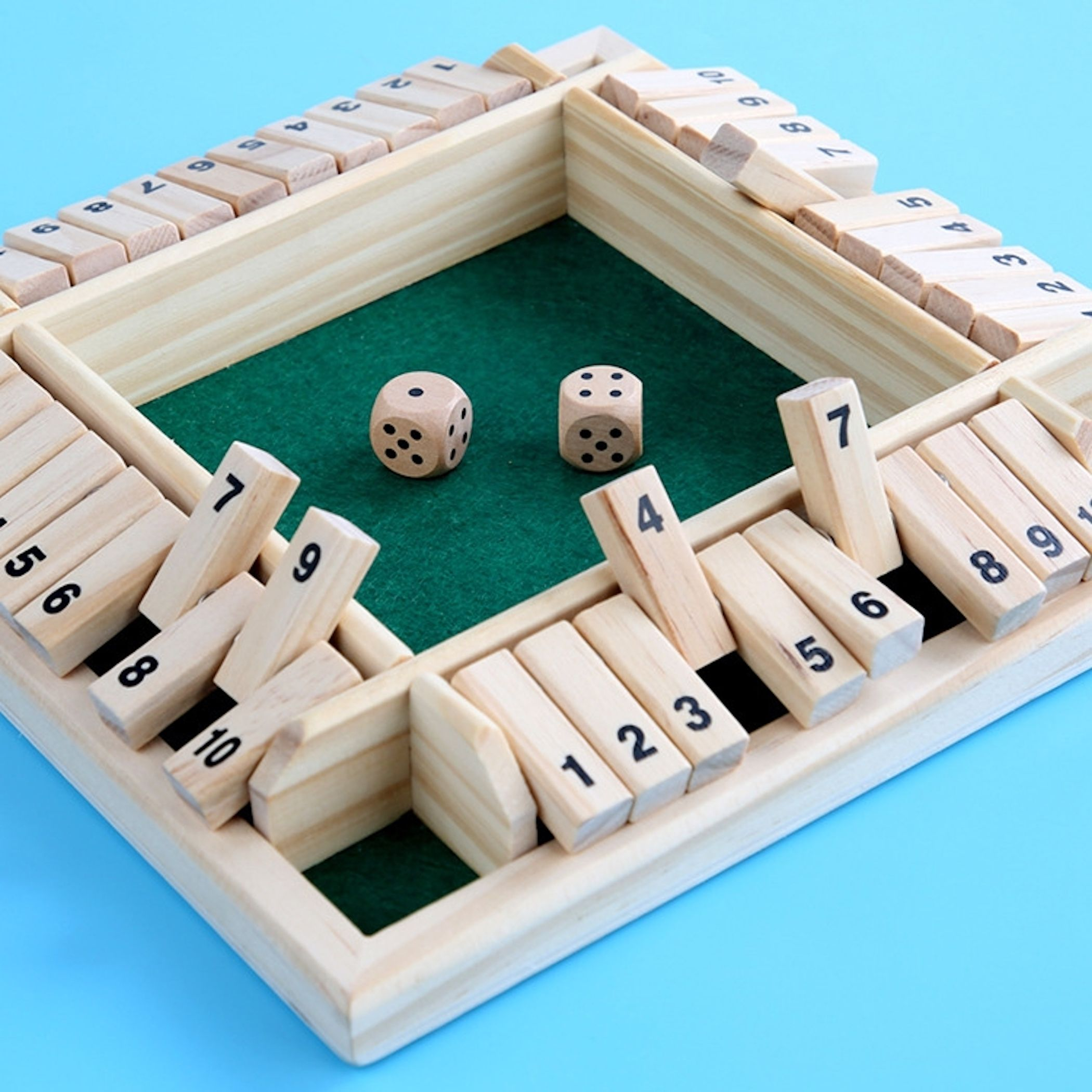 Ein hölzernes Shut-the-Box-Spiel mit grünem Filz im Inneren und zwei Würfeln auf einem blauen Tisch.