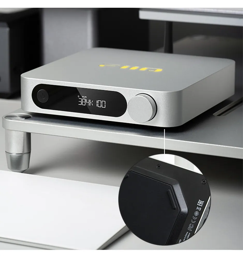 Reproductor de audio plateado con pantalla digital y control de volumen en soporte.