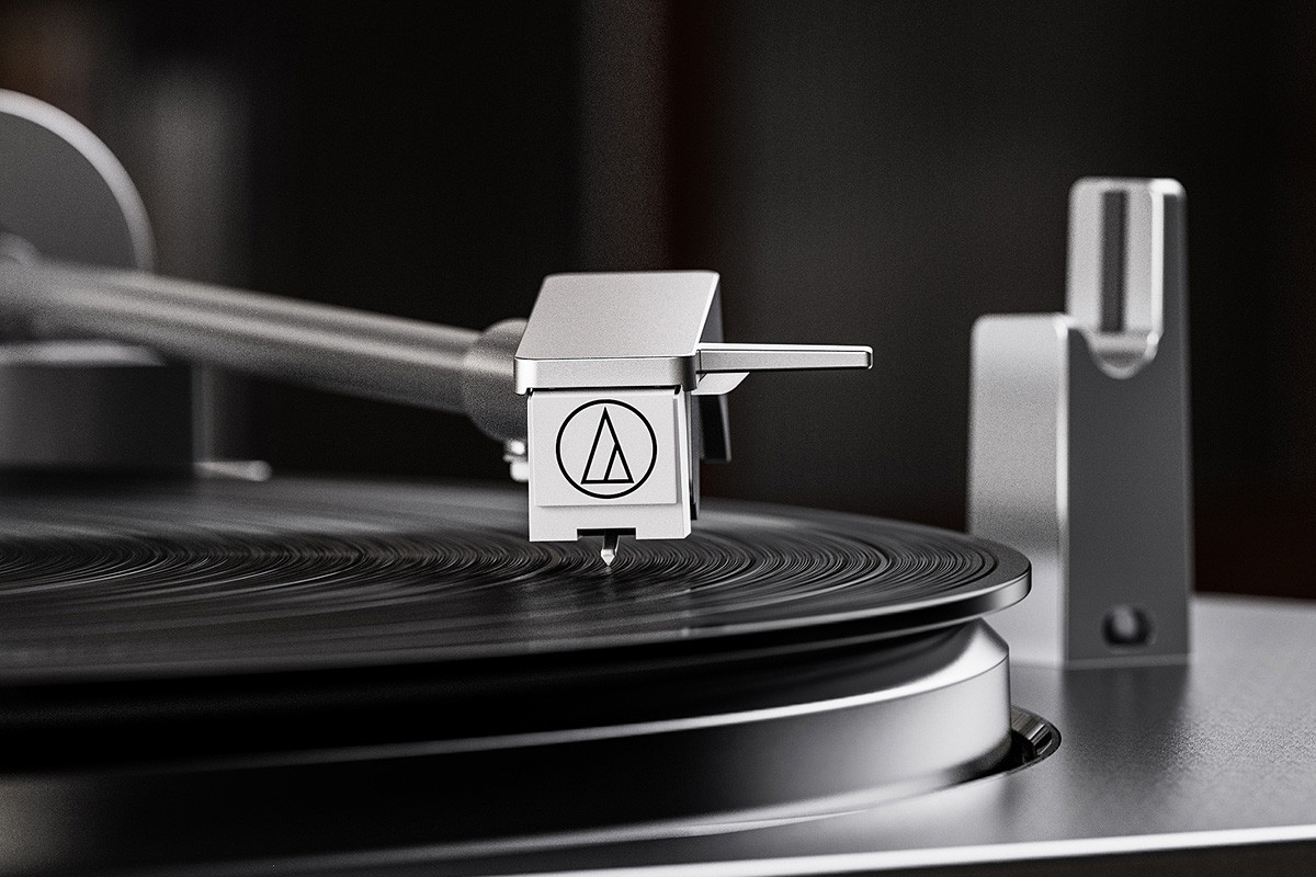 Primer plano de una cápsula de tocadiscos sobre un disco de vinilo negro, con brazo metálico y fondo oscuro.