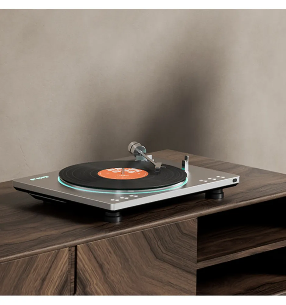 Un tocadiscos moderno plateado con un disco de vinilo negro sobre un mueble de madera ante una pared beige.