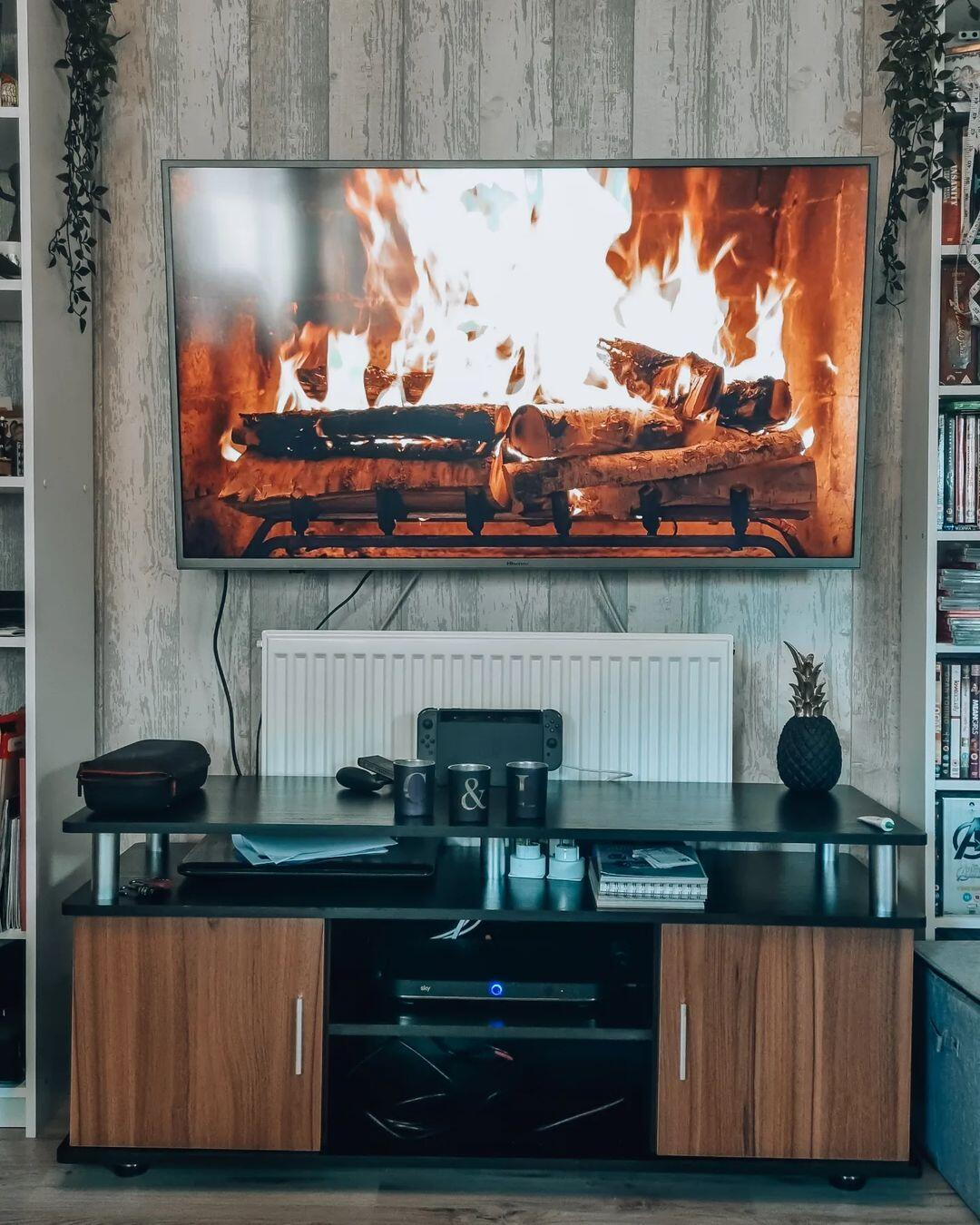 Una TV con un camino su una parete in legno sopra un mobile nero con ripiani e ante.