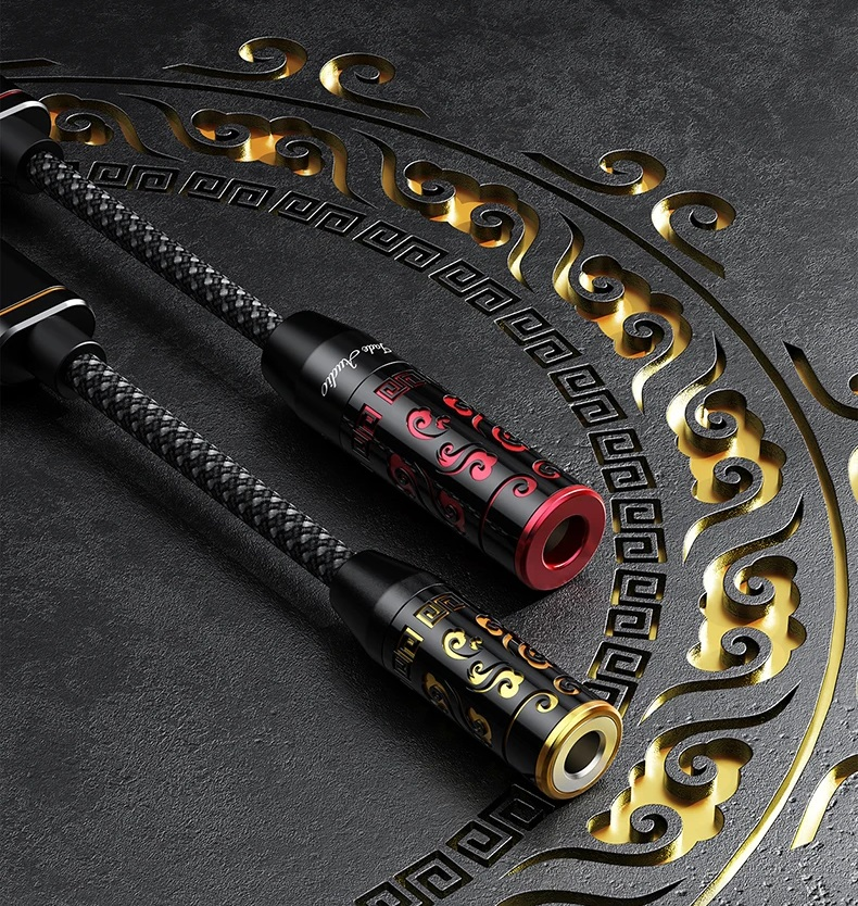 Due cavi audio intrecciati con spine decorate poggiano su una superficie scura incisa con motivi dorati.