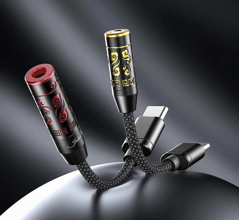 Due adattatori da USB-C a jack audio con cavi intrecciati neri e motivi decorati su un piedistallo scuro.