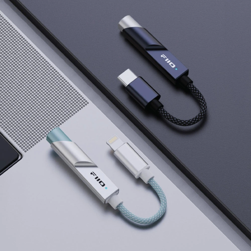 Dos cables adaptador FiiO con cordones trenzados reposan sobre una superficie plateada y negra.