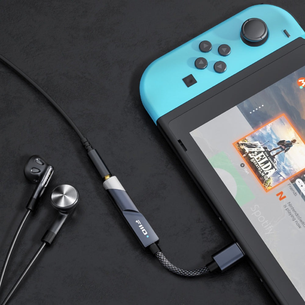 Un adaptador de audio negro conecta auriculares con cable a una consola Nintendo Switch.