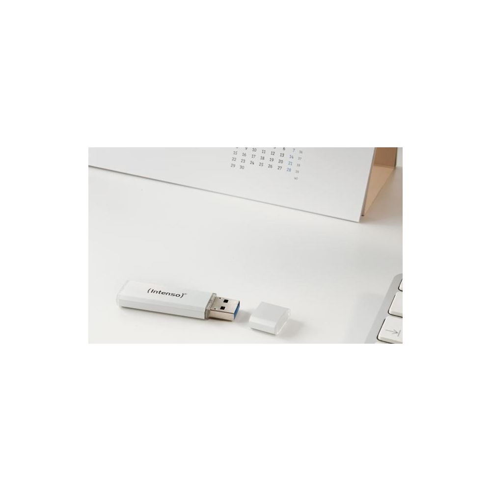Una unidad flash USB Intenso blanca con la tapa quitada en una mesa blanca, con un calendario de fondo.