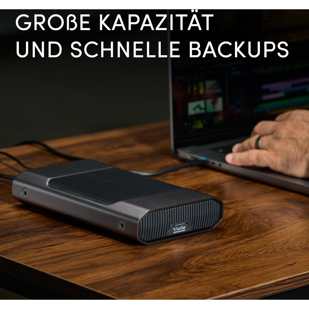 Un disco duro profesional SanDisk oscuro está en un escritorio de madera junto a una computadora portátil.
