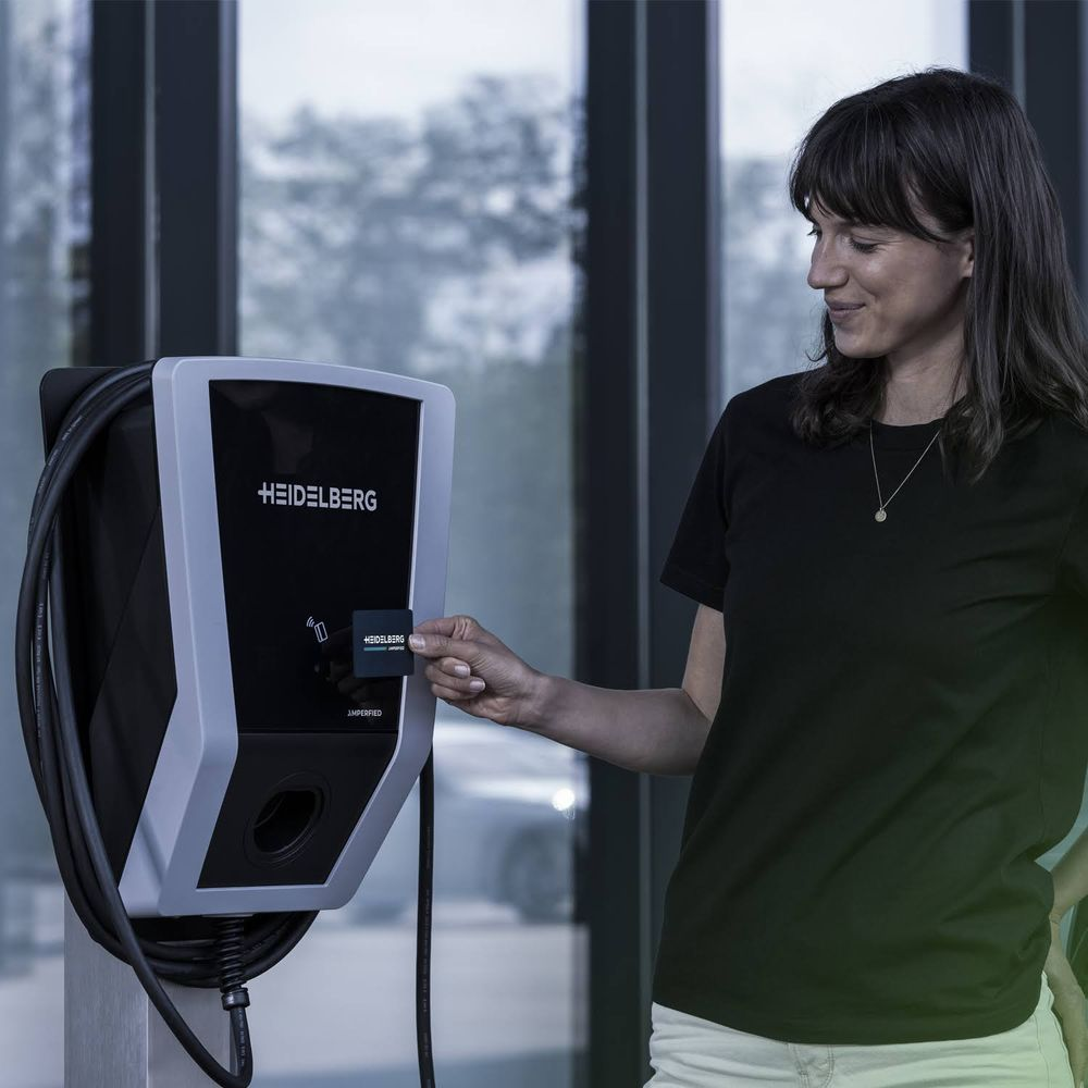 Eine Frau hält eine Ladekarte an eine weiße Heidelberg Wallbox.