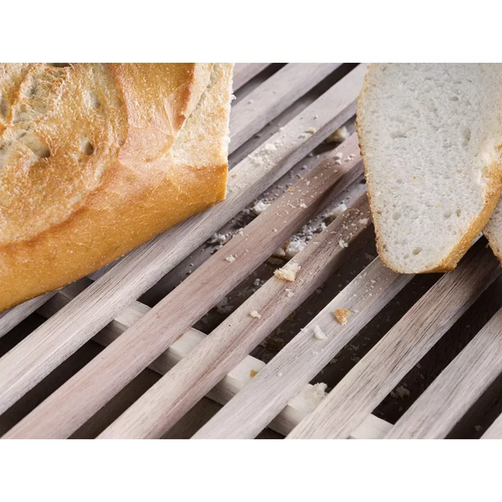 Ein Laib Brot und Scheiben liegen auf einem Holzlattenschneidebrett mit verstreuten Krümeln.