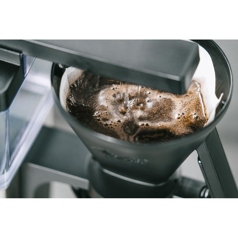Wasser gießt in einen Kaffeefilter mit frisch gebrühtem Kaffee in einer Kaffeemaschine.