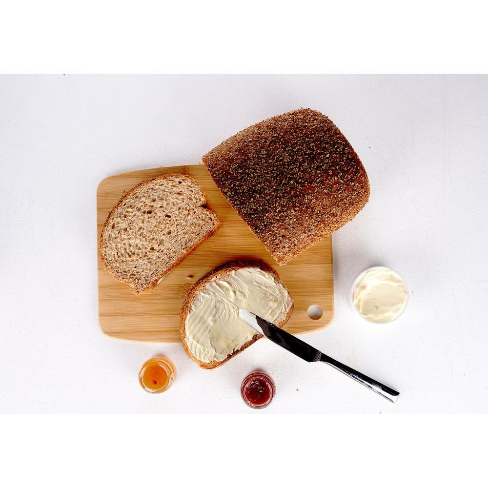 Ein Laib braunes Brot und Scheiben auf einem Holzbrett mit Butter und kleinen Gläsern Marmelade.