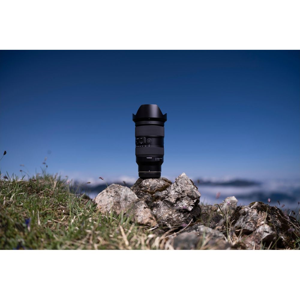 Un obiettivo fotografico è in equilibrio sulle rocce in cima a una montagna erbosa sotto un cielo azzurro.