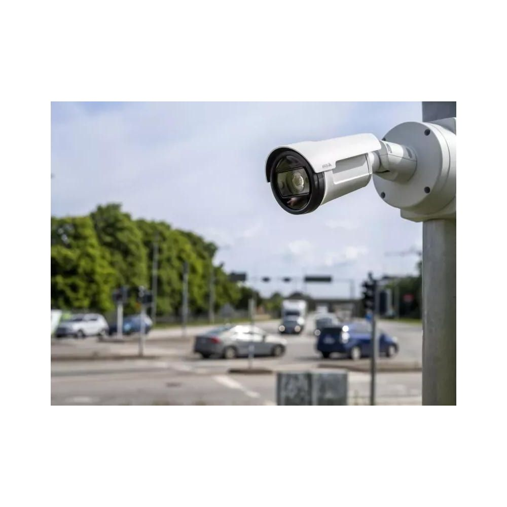 Eine weiße Überwachungskamera ist an einer Stange montiert, im Hintergrund ist eine verkehrsreiche Straße zu sehen.