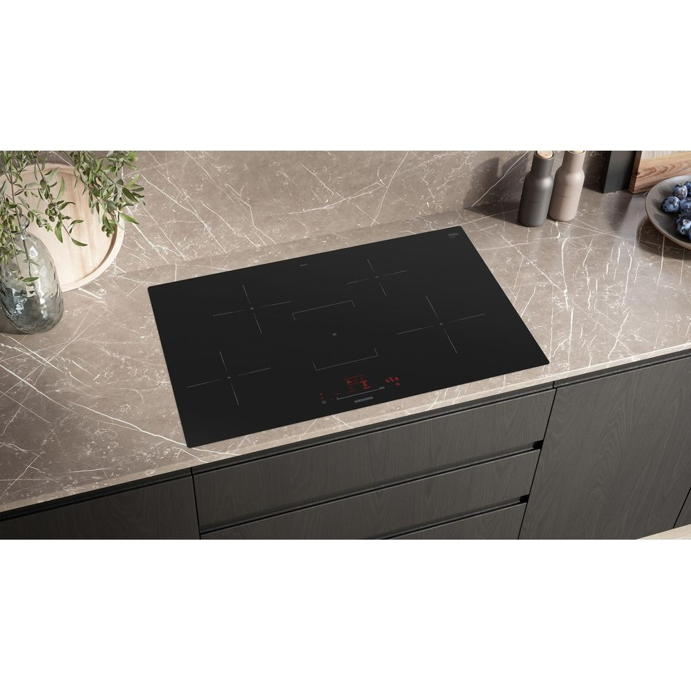 Plaque à induction noire sur plan de travail en marbre dans une cuisine moderne avec plantes et épices.