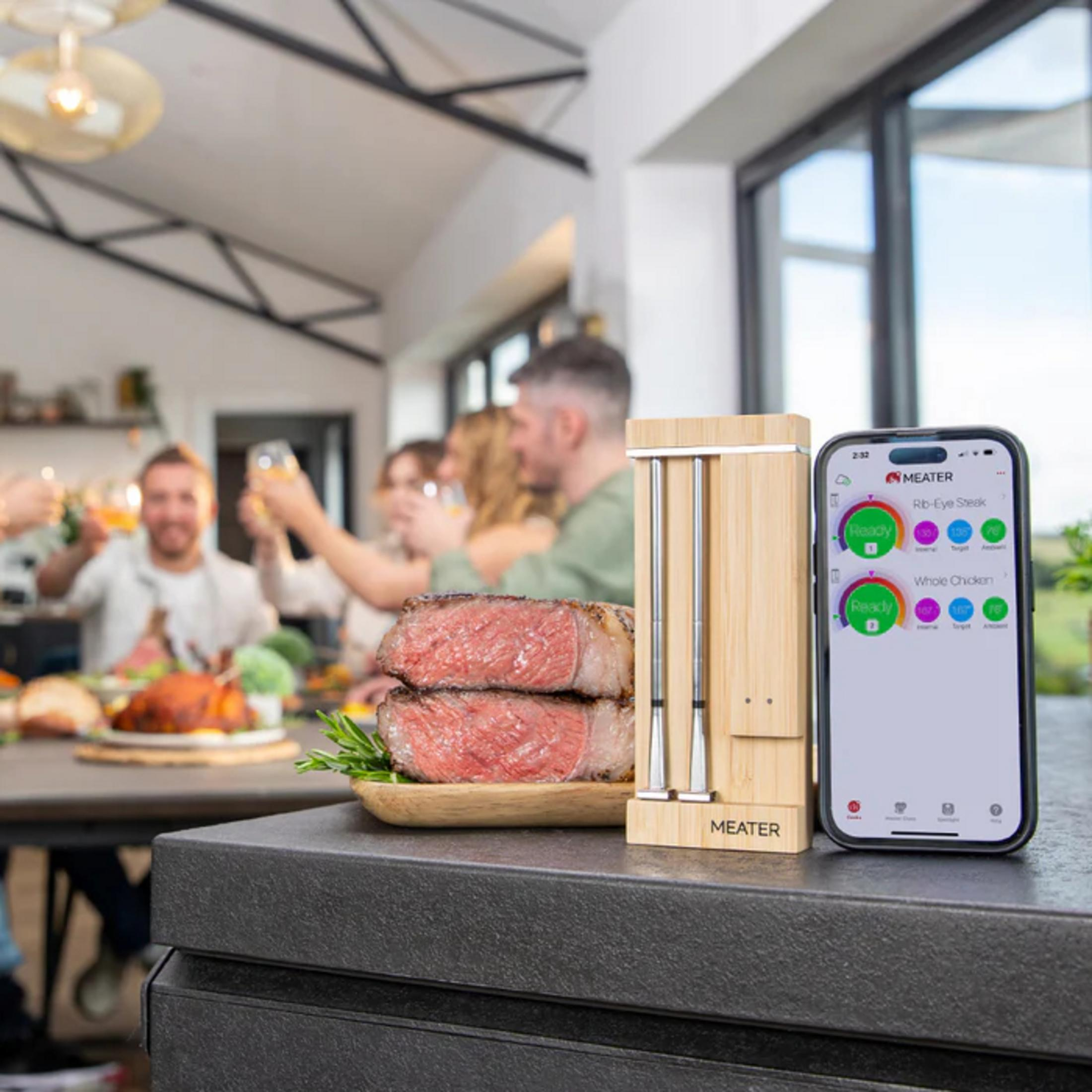Un thermomètre à viande Meater et une application affichent la cuisson de deux steaks, avec des invités en arrière-plan.