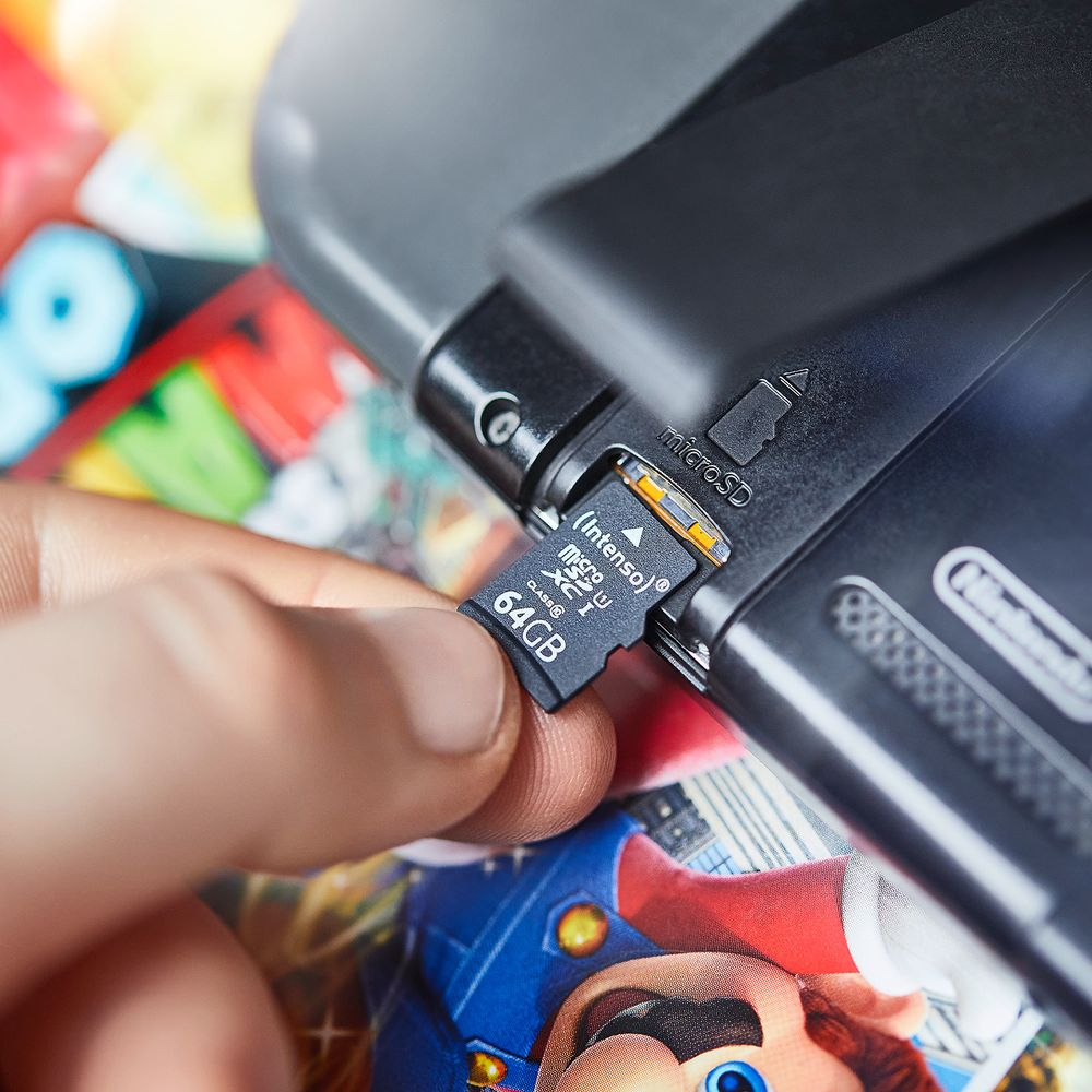Une main insère une carte microSD Intenso de 64 Go dans une console.