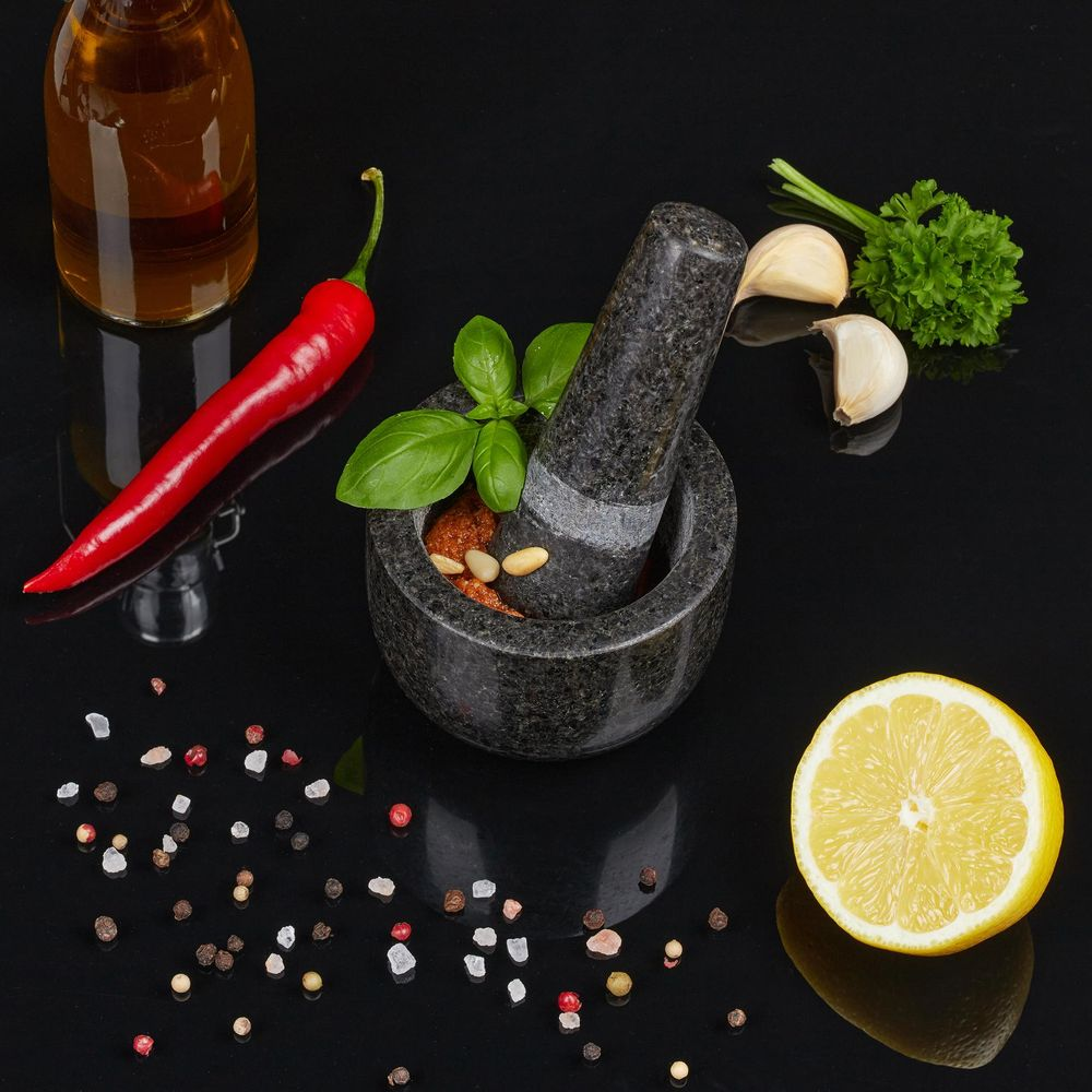 Mörser mit Pestozutaten, Chili, Knoblauch, Zitrone und Gewürzen auf schwarzem Hintergrund.