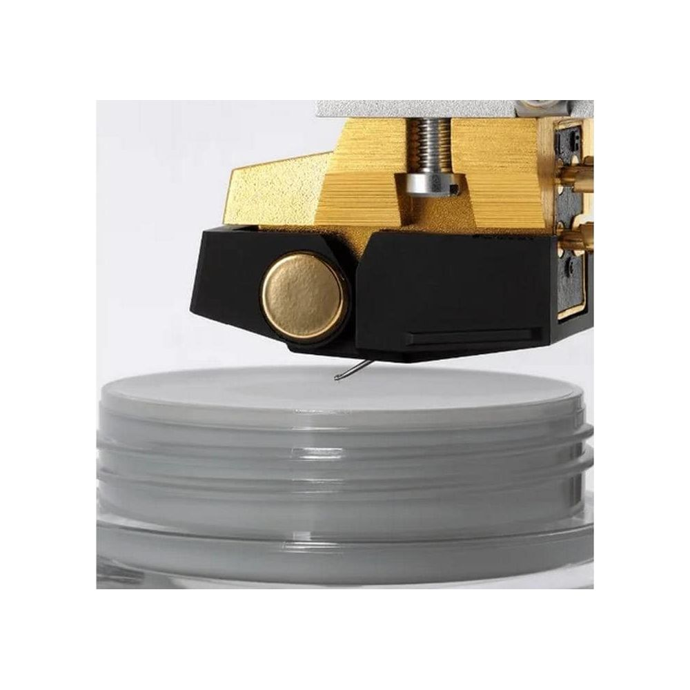 Un cartucho de tocadiscos dorado y negro con una aguja visible sobre una superficie gris.
