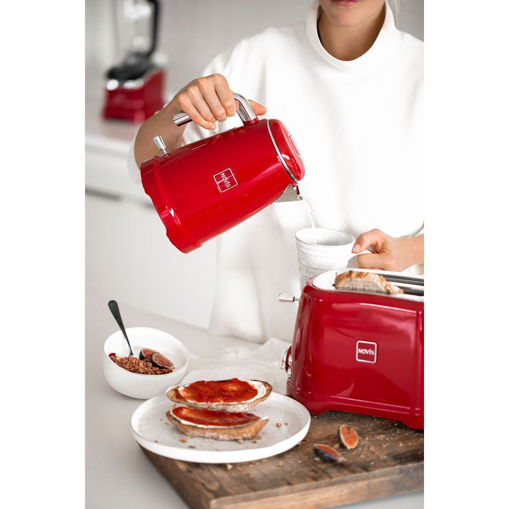 Eine Person gießt Wasser aus einem roten Wasserkocher in eine Tasse, neben Toast und einer Schüssel.
