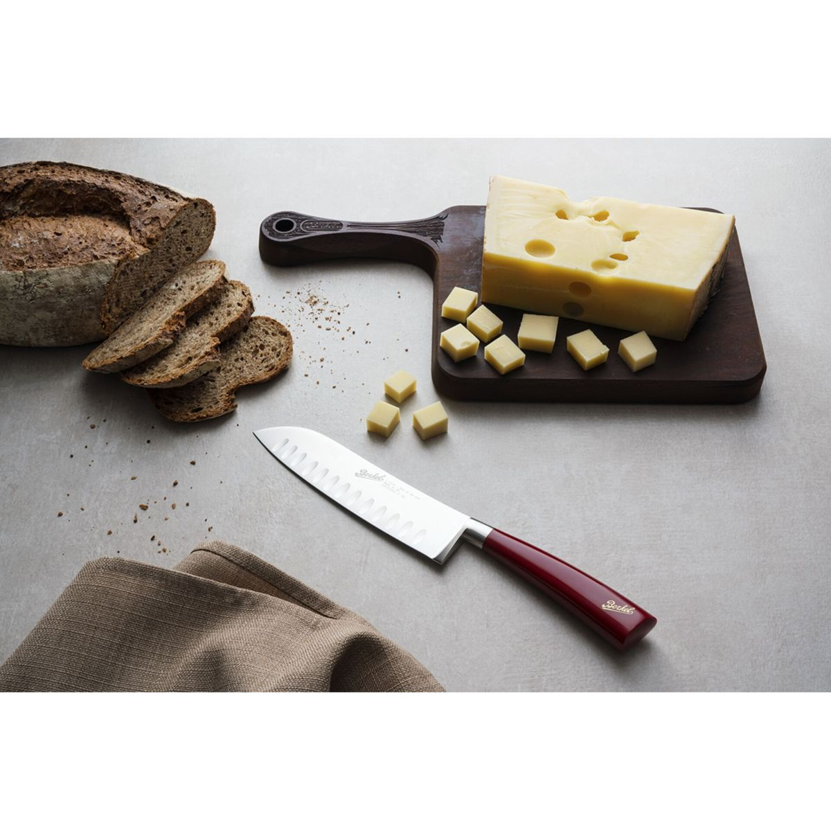 Pane affettato e formaggio su un tagliere di legno con un coltello dal manico rosso sulla superficie grigia.