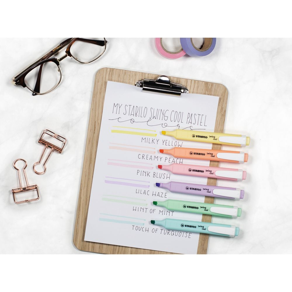 Klemmbrett mit Pastell-Textmarker, Brille und Büroklammern auf Marmoroberfläche.