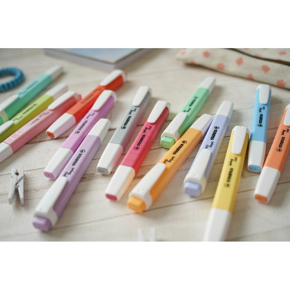 Viele bunte Textmarker liegen auf einem hellen Holztisch neben Schreibwaren.