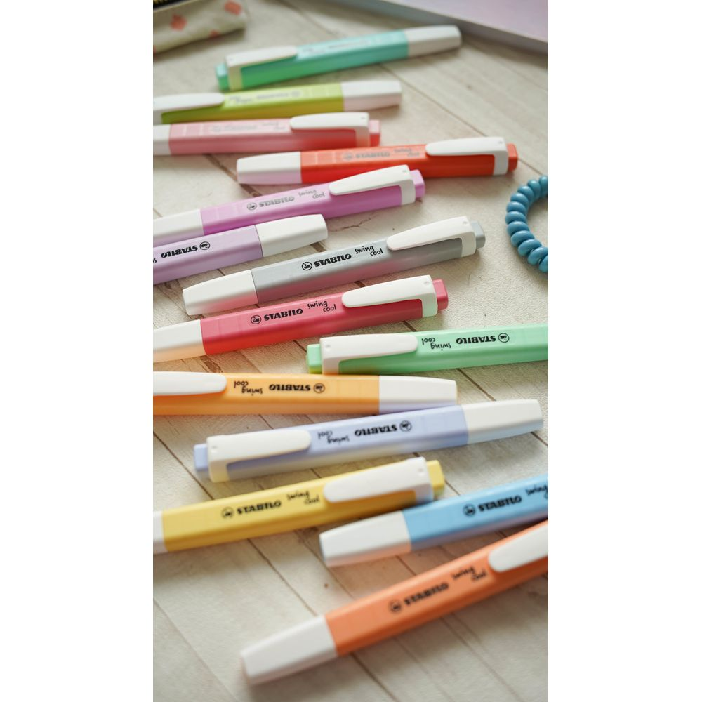 Viele bunte Stabilo Swing Cool Textmarker liegen auf einer Holzoberfläche.