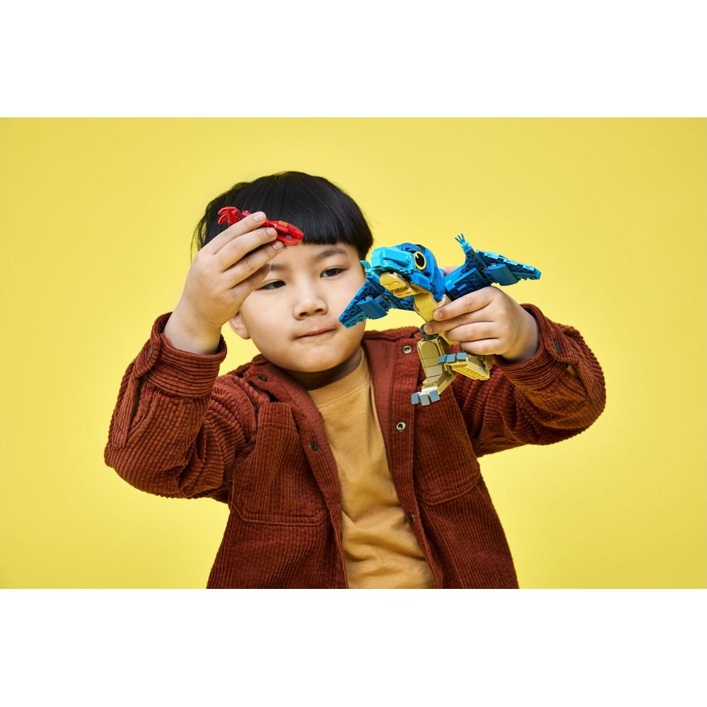 Un bambino con una giacca marrone gioca con due piccoli dinosauri giocattolo blu e rossi su sfondo giallo.