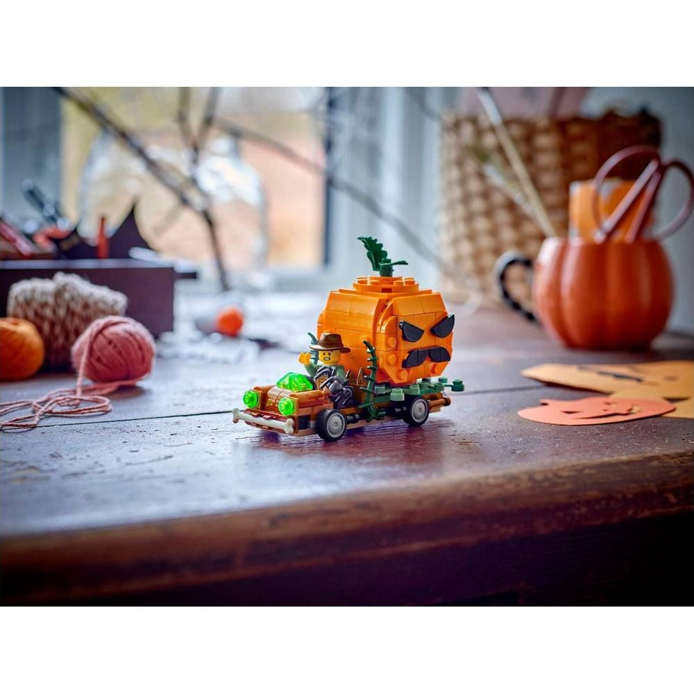 Una minifigura Lego guida un'auto giocattolo che trasporta una grande zucca arancione con una faccia spaventosa.
