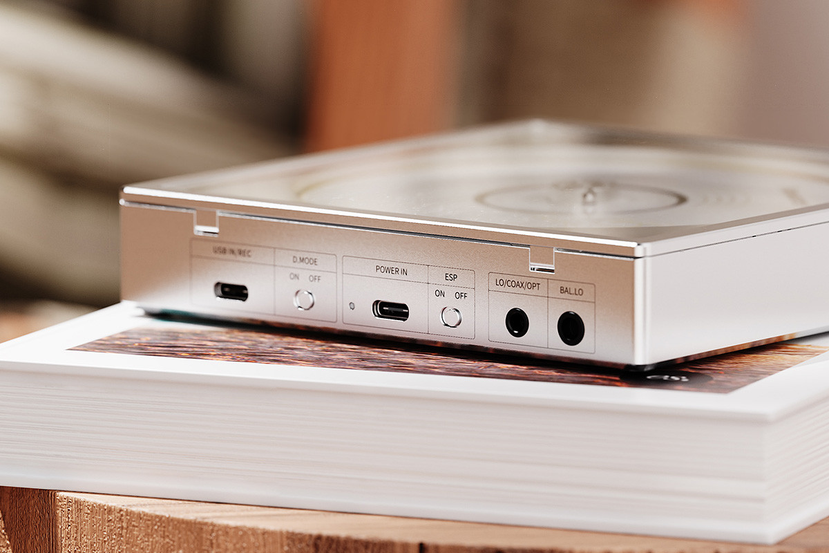 Dispositivo de audio plateado con puertos en el panel lateral, colocado sobre un libro.