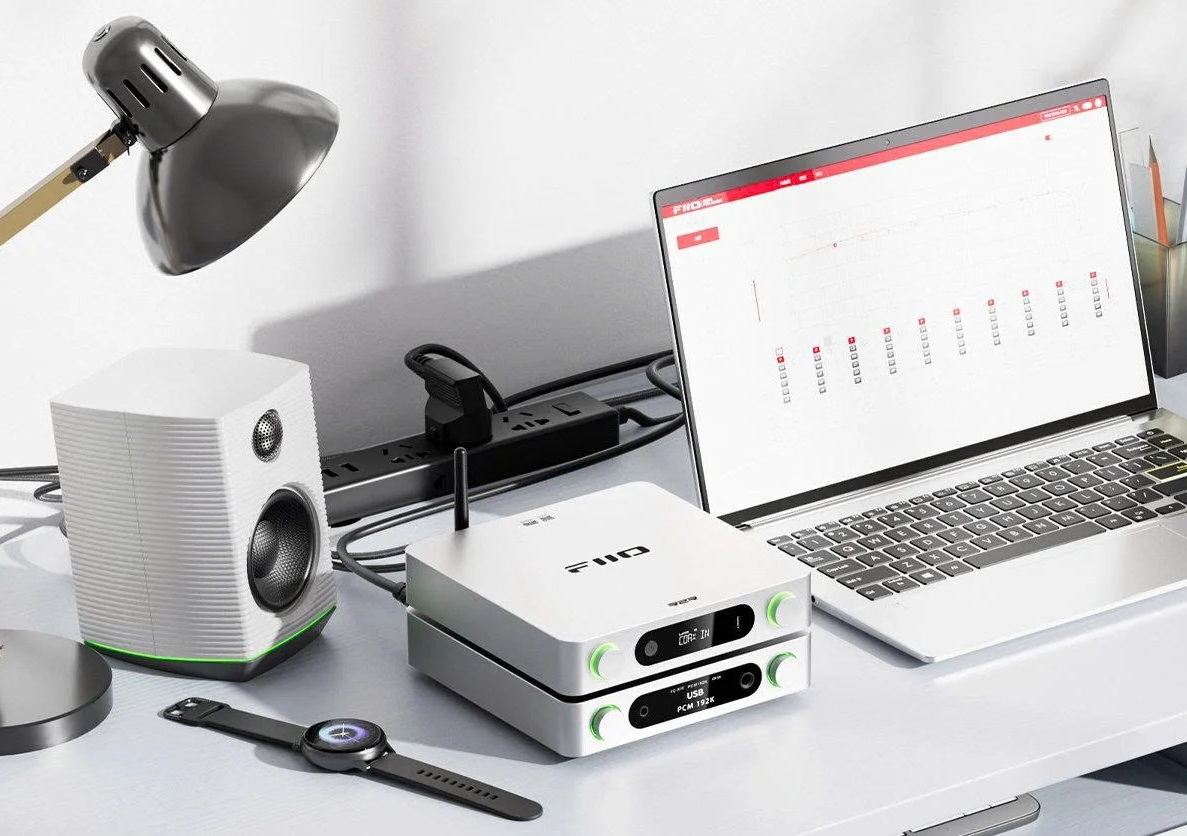 Un dispositivo de audio FiiO, una computadora portátil, un altavoz y un reloj están en un escritorio.