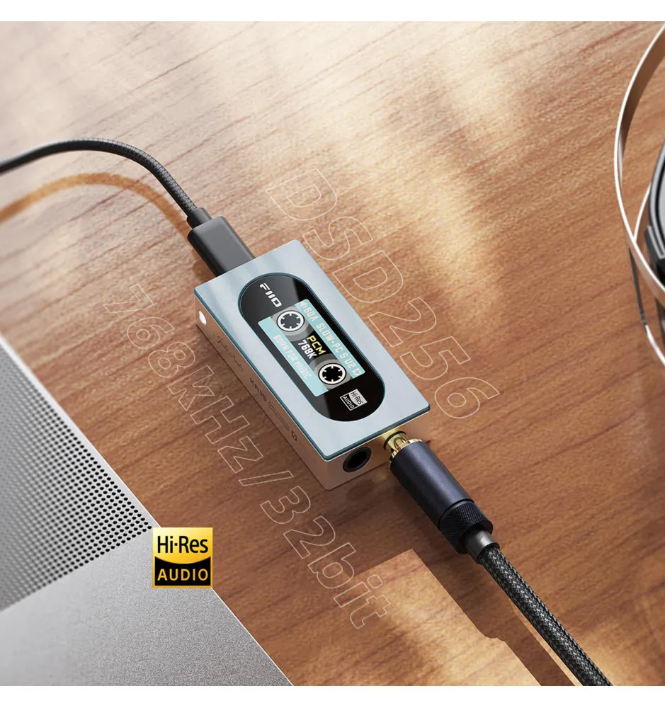 Un amplificador de audio DAC portátil plateado conectado a cables en una mesa de madera.