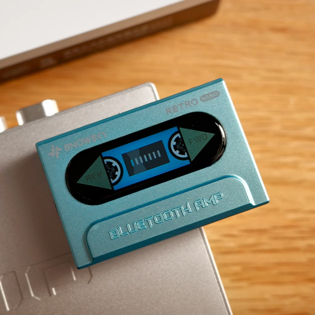Un amplificador Bluetooth Retro Nano azul con diseño de casete sobre una superficie plateada y de madera.