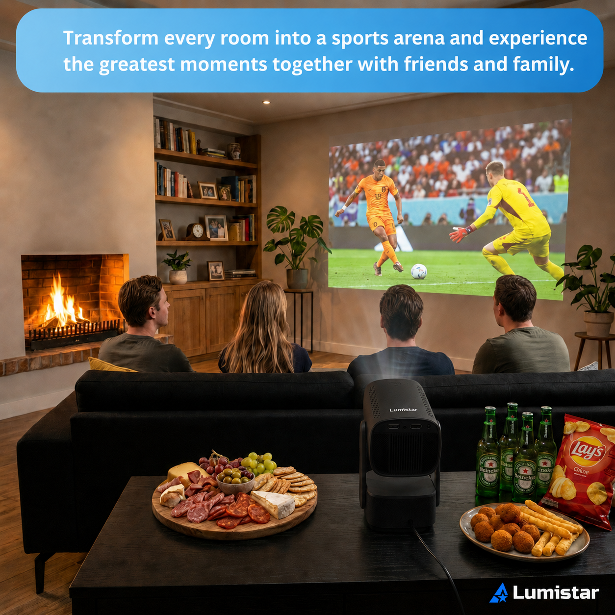 Vier Personen sitzen vor einer Leinwand, auf der ein Fußballspiel läuft, auf dem Tisch liegen Snacks und Getränke.