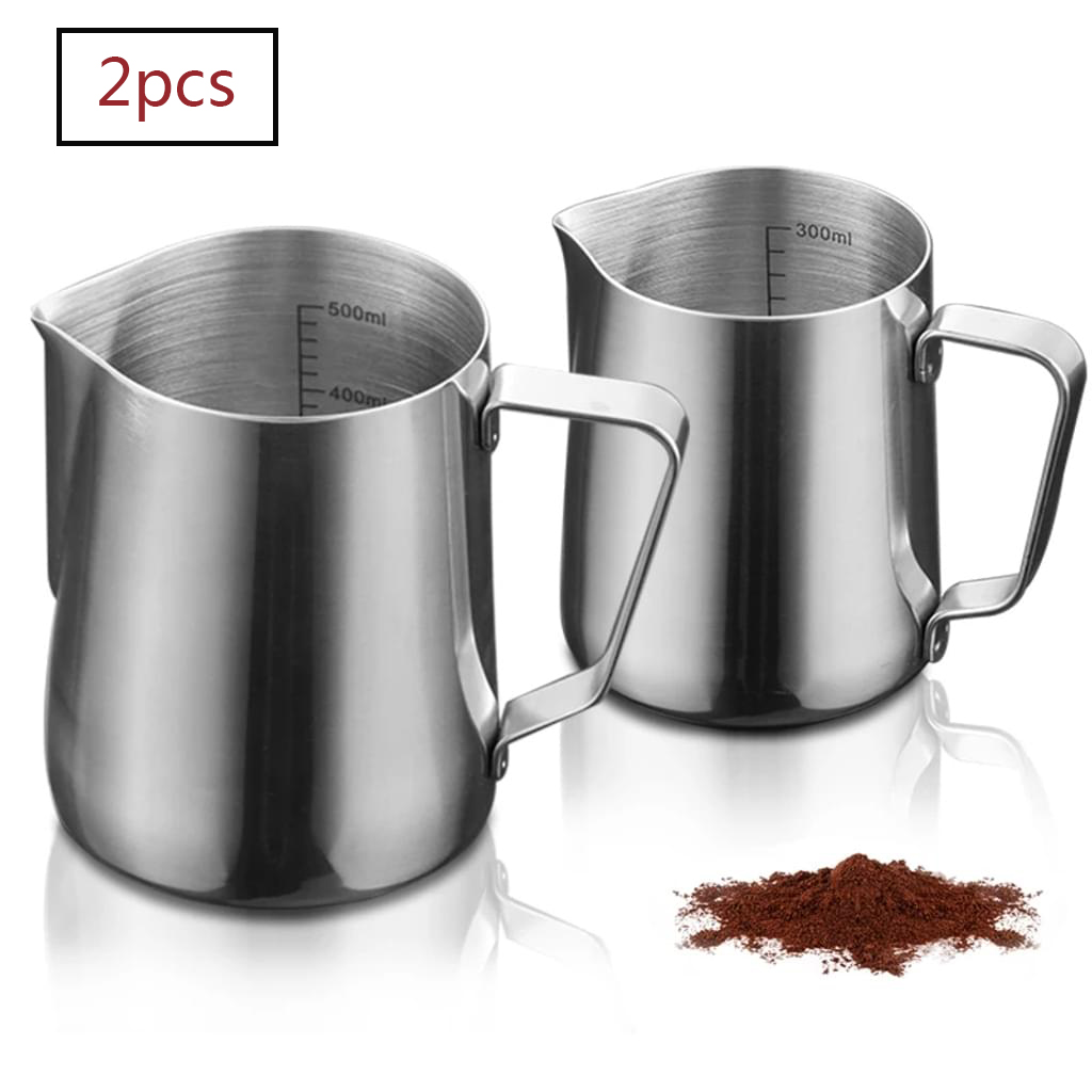 Zwei silberne Edelstahl-Milchaufschäumkännchen mit Messmarkierungen und Kaffeepulver auf weißem Hintergrund.