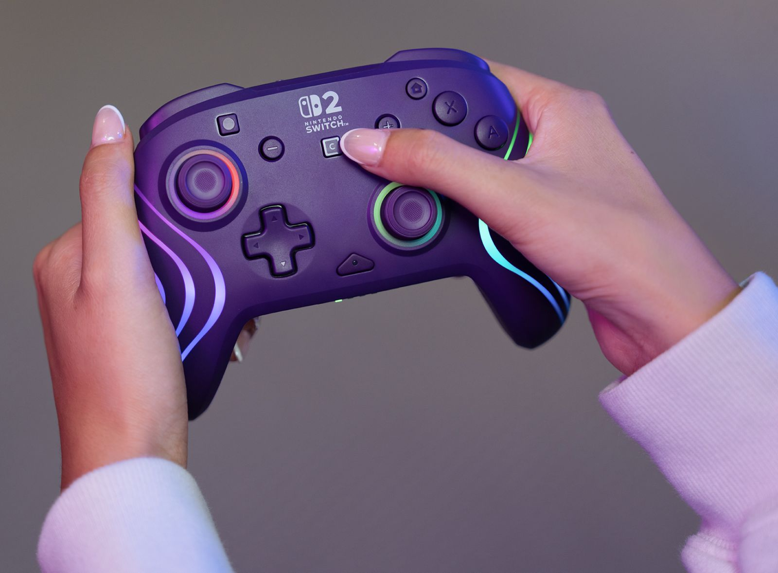 Mains tenant une manette de jeu violette avec un éclairage coloré.