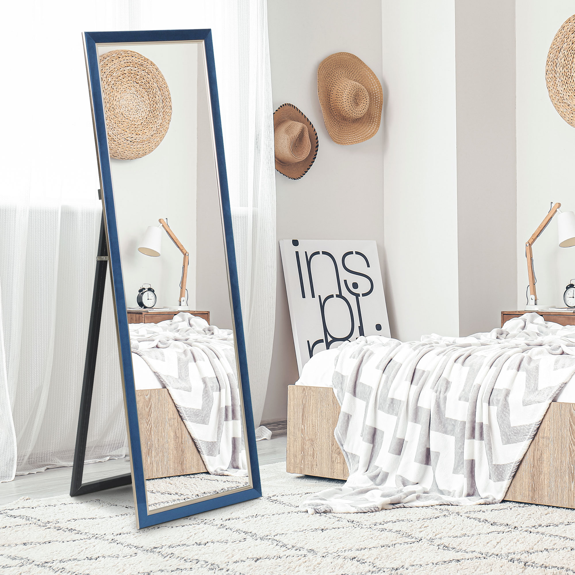 Un gran espejo de suelo con marco azul se encuentra en un dormitorio acogedor con sombreros y cama.