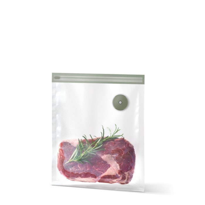 Un trozo de carne cruda con romero está envasado al vacío en una bolsa sellable sobre fondo blanco.