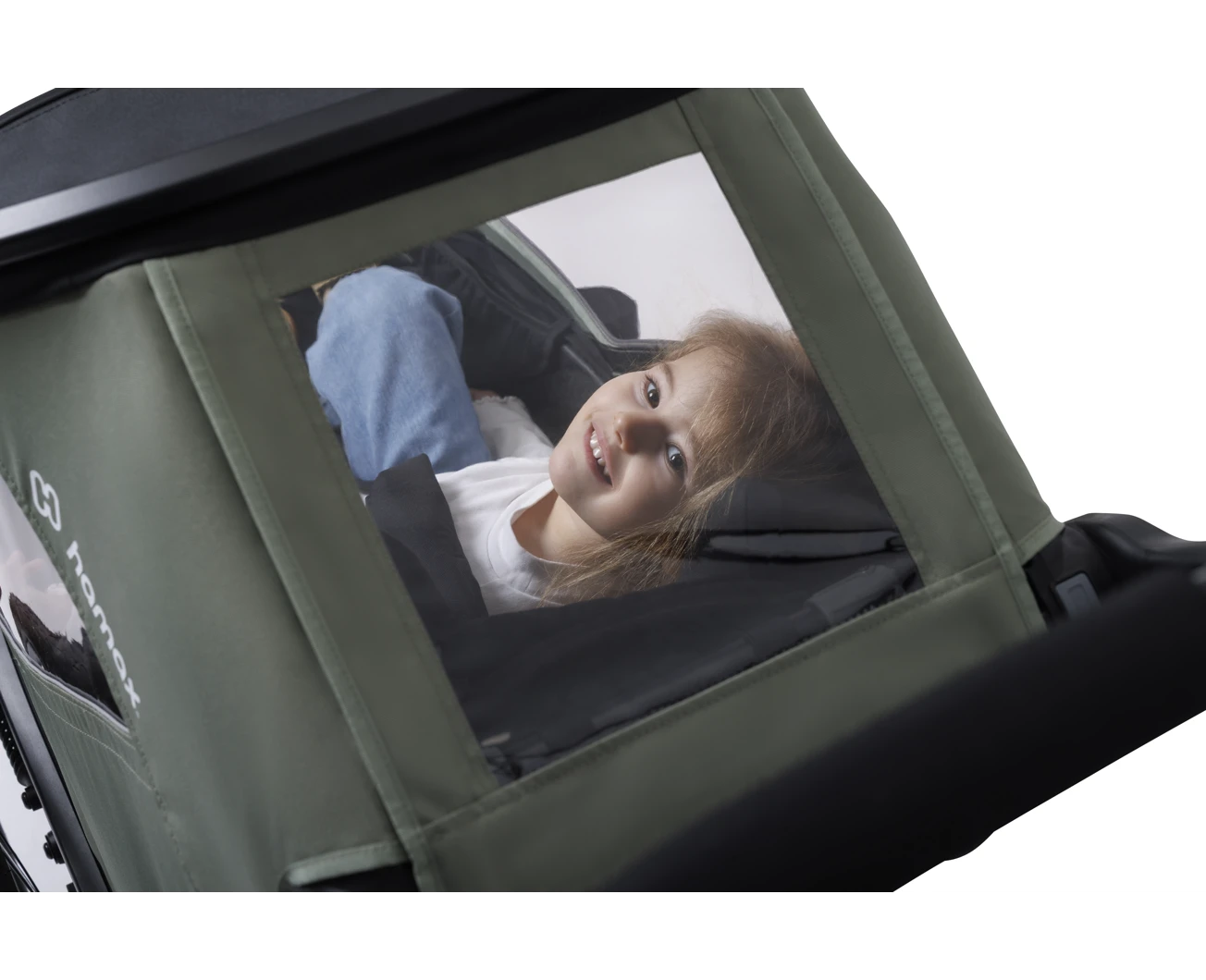 Una niña sonríe dentro de un remolque infantil verde oliva y negro, vista a través de la ventana lateral abierta.