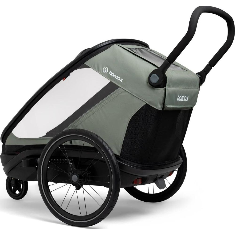 Un remolque de bicicleta para niños gris con ruedas negras y manillar curvo sobre fondo blanco.